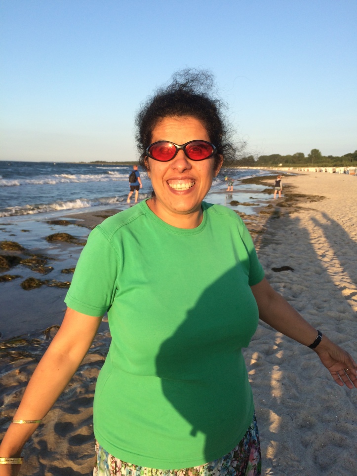 Lydia am Strand mit ausgebreiteten Armen, grünes T.Shirt und buntem Rock